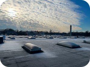 Mehrere Solaranlagen, die auf einem grauen Flachdach angebracht wurden. Die Sonne scheint durch die Wolken.