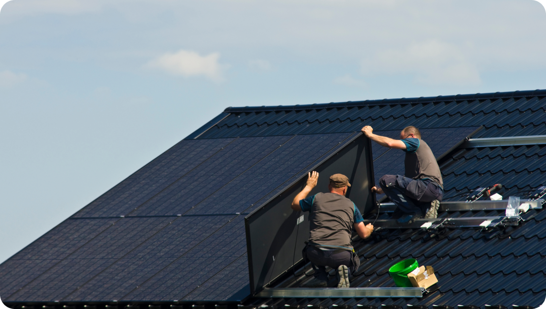 Zwei Mitarbeiter bringen eine Solaranlage auf einem schwarzen Dach an