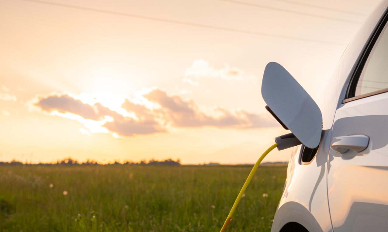 Weißes E-Auto steht bei Sonnenuntergang an einer Wiese und lädt auf