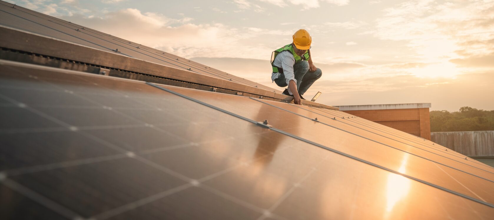 Person mit Helm befindet sich bei Sonnenuntergang auf einem Dach und bringt Solaranlagen an